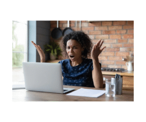 Person sitting in front of open laptop, with hands up, looking angry