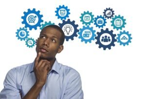A thoughtful young man in a blue shirt looking up, surrounded by illustrated gears and icons representing ideas, planning, teamwork, and digital tools