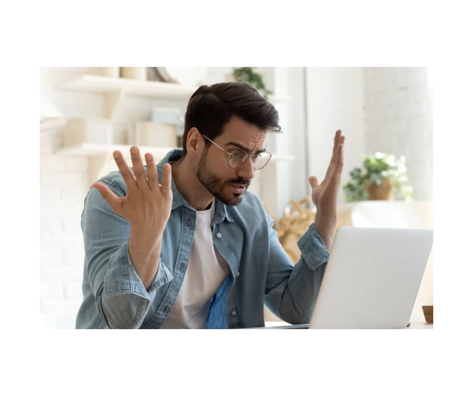 A person sitting at a table with their hands up in front of their laptop, looking worried